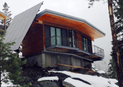 Finished cabin, side view, on steep mountain side, features solar panels.